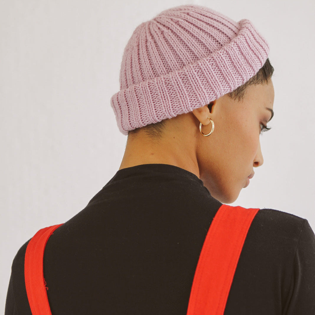 Person wearing a pink knit beanie and red apron over a black shirt on a white background