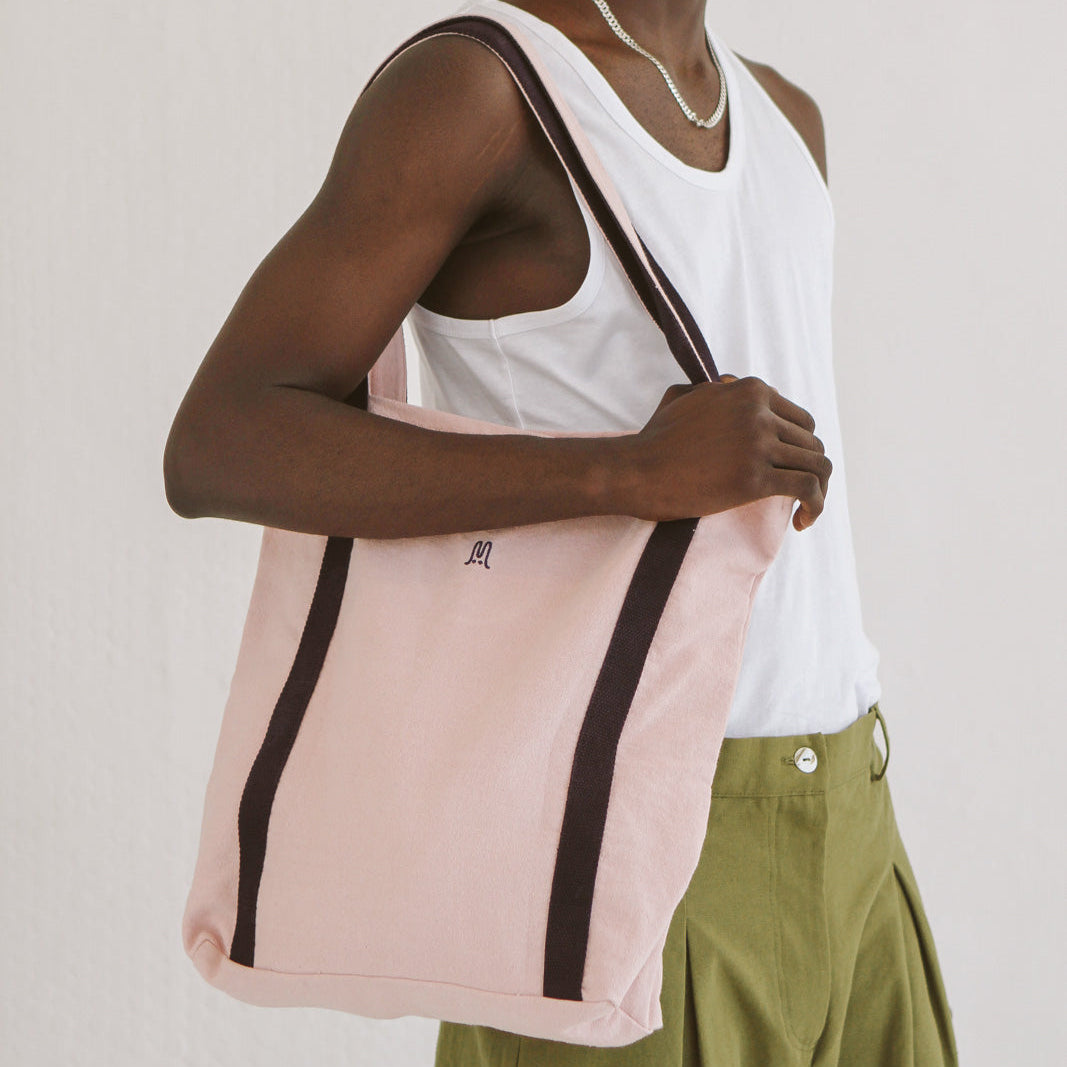 Person holding a pink tote bag with a black stripe against a plain background