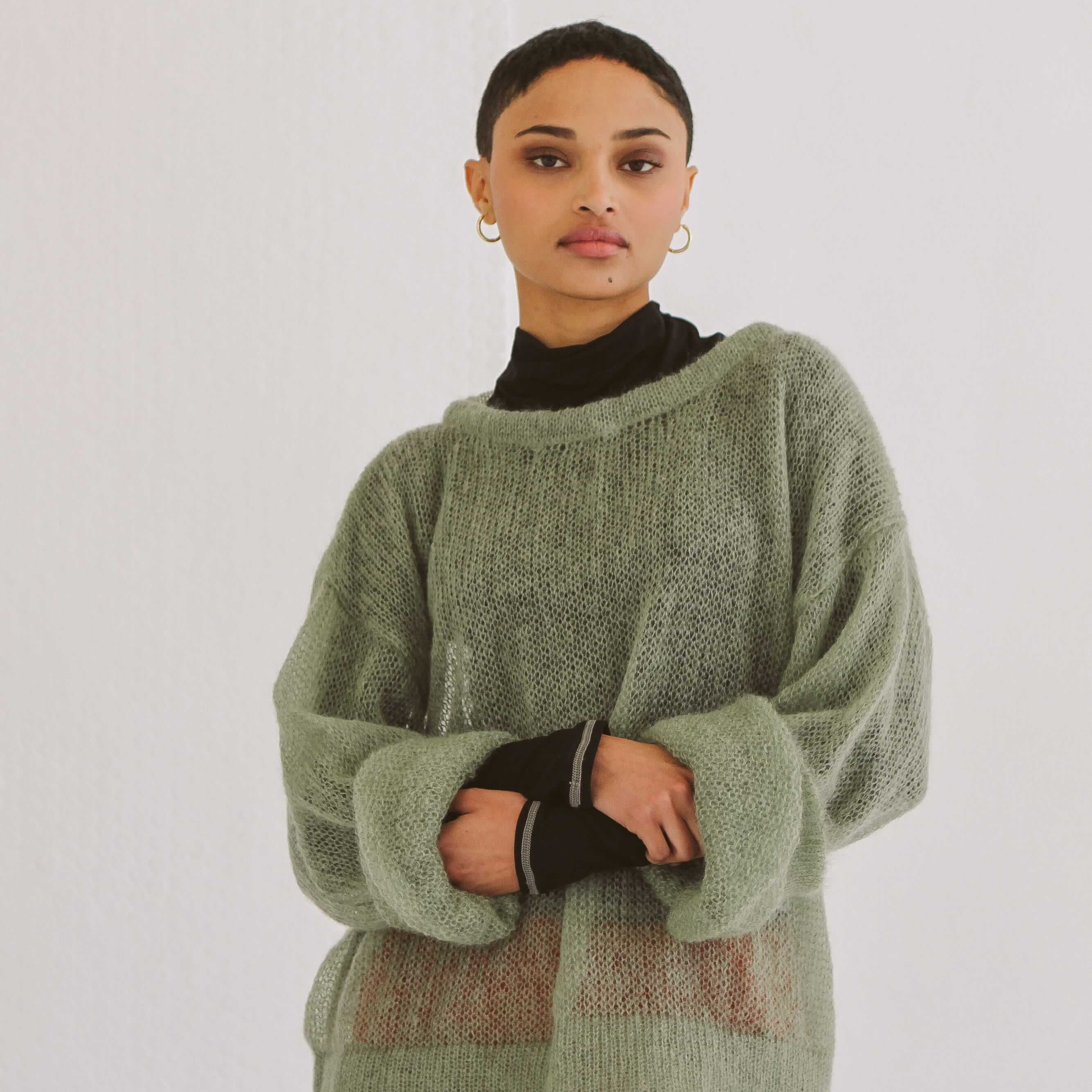 Woman wearing a green sweater over a black turtleneck with a red skirt on a white background