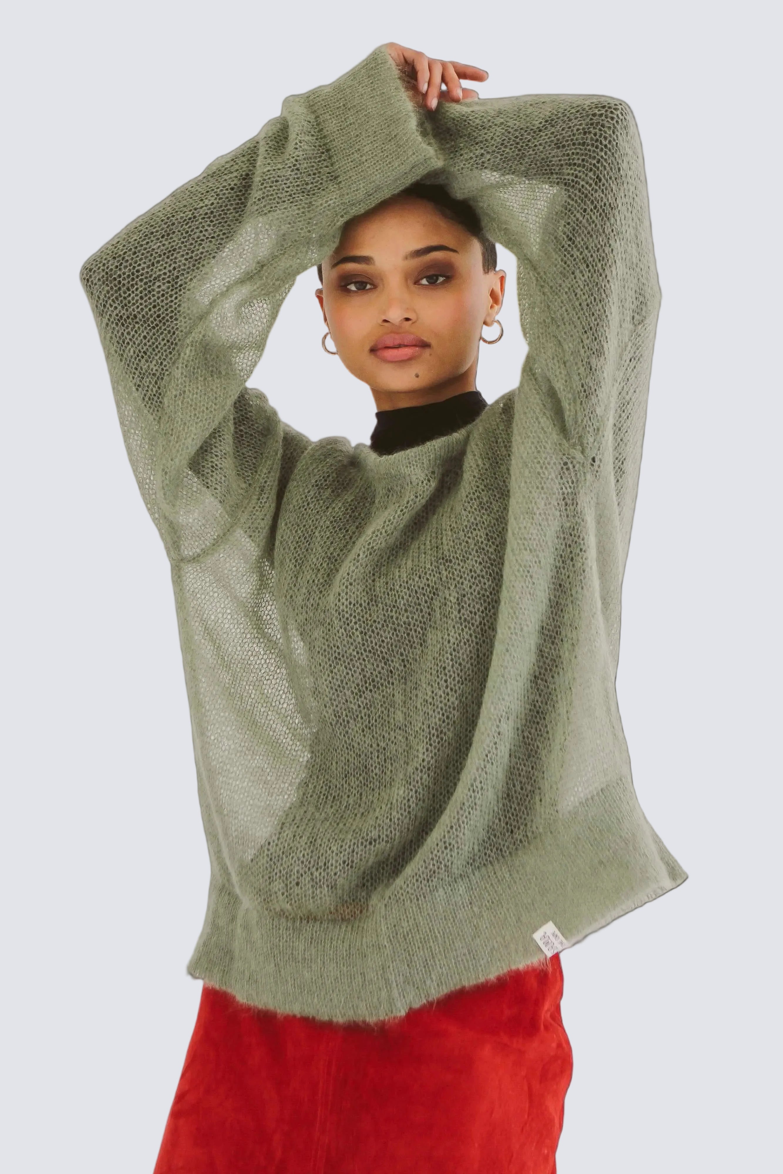 Person wearing a green mohair knit sweater and red pants against a white background