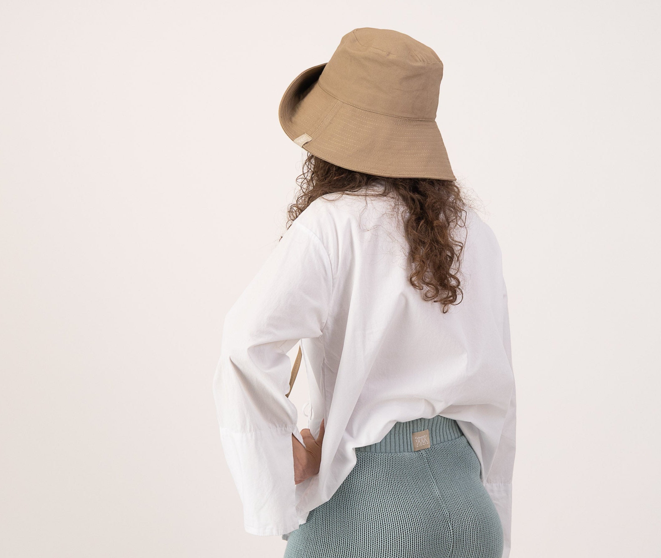 Person wearing a white shirt, light blue shorts, and a beige hat on a plain background