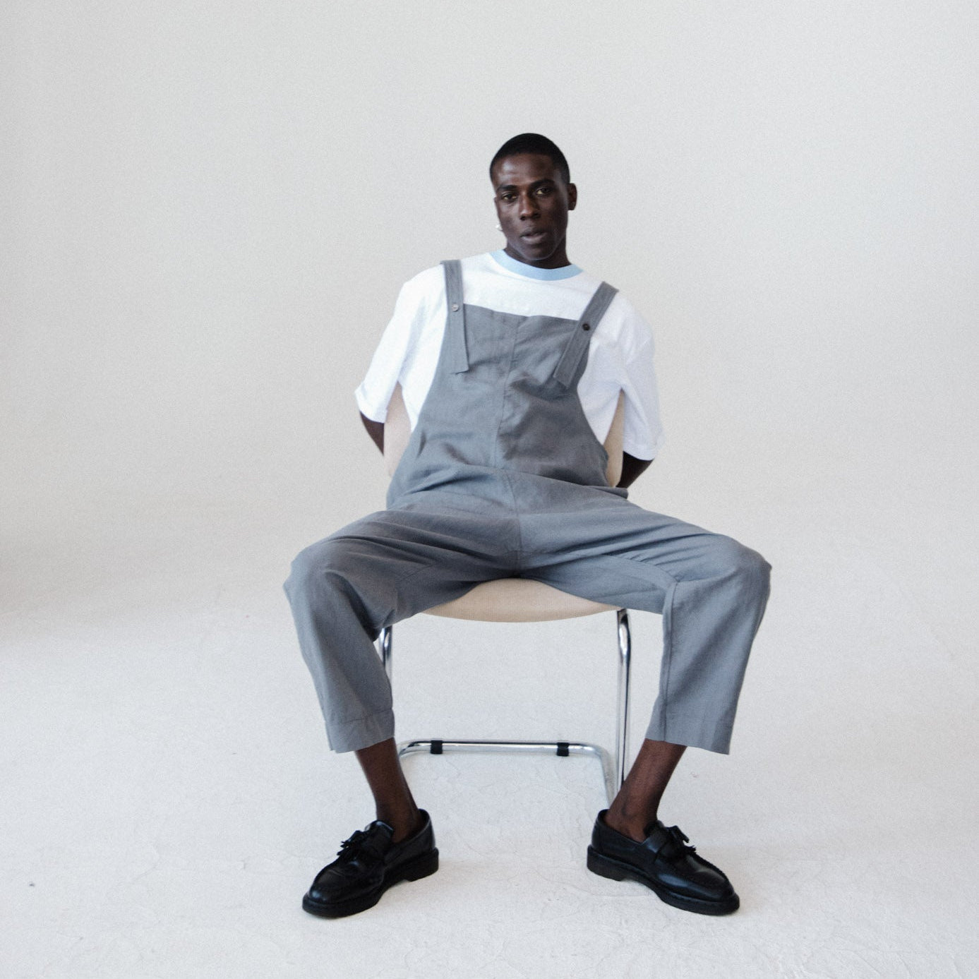 Person wearing gray overalls sitting on a chair against a white background